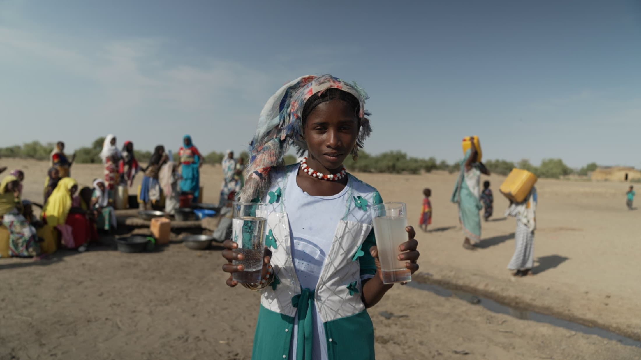 Girl holding clean and unsafe water containers in a rural community