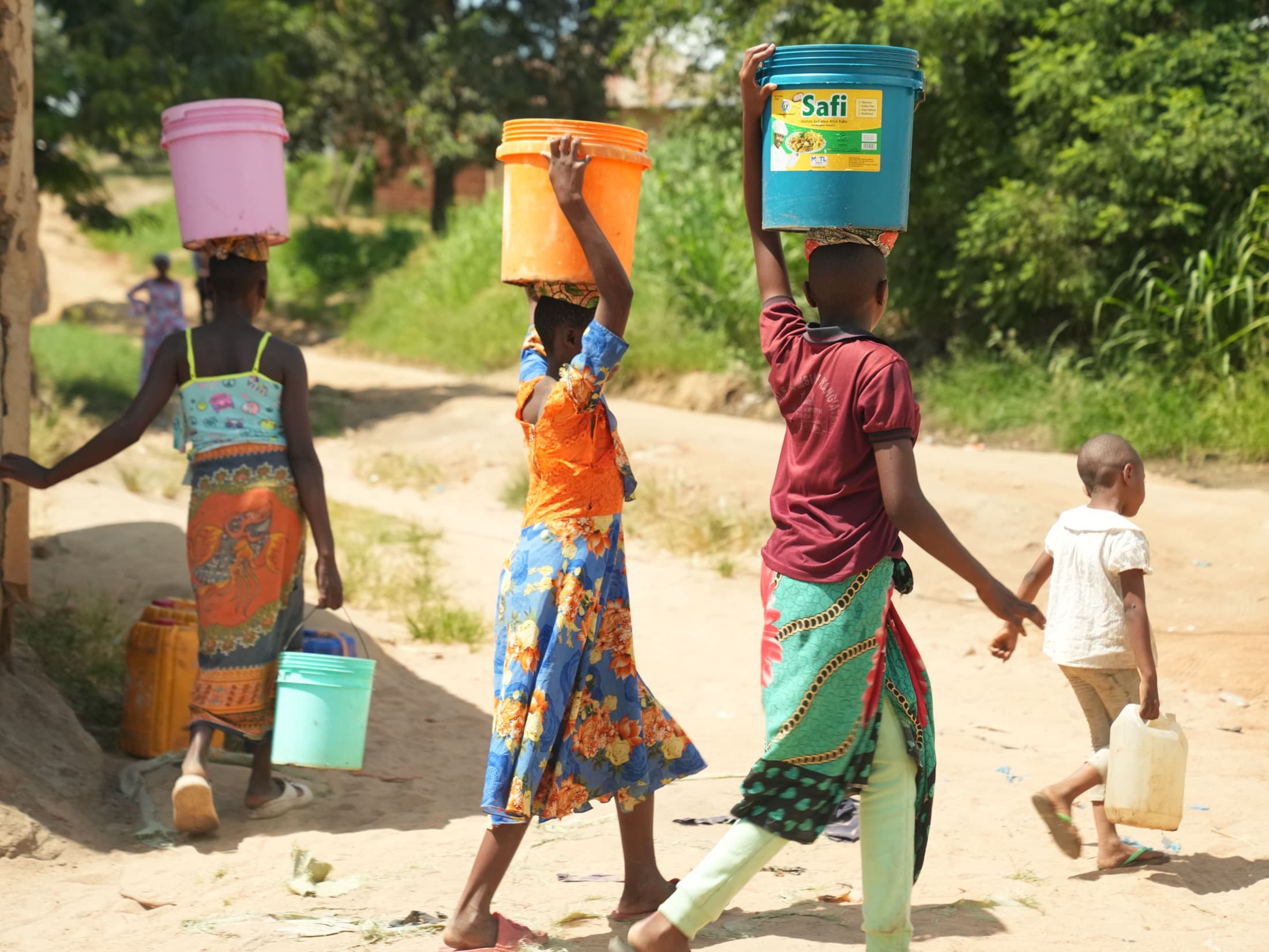 Women and children carrying water containers along a rural road