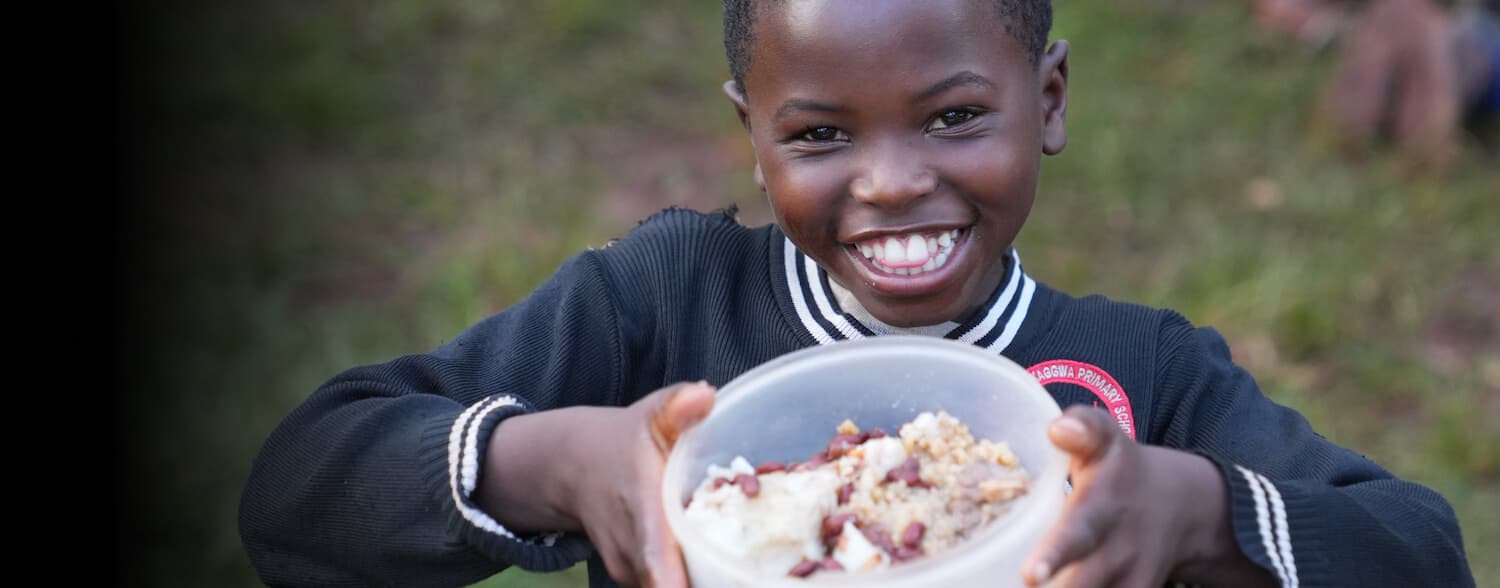 An orphaned child smiling while holding a bowl of food